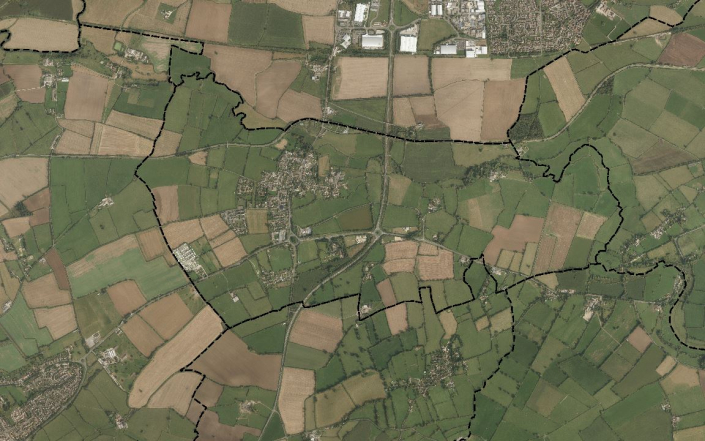 A satellite view of a rural area with patchwork fields, small clusters of buildings, and winding roads. Black dashed lines outline different sections of the landscape, possibly indicating boundaries.